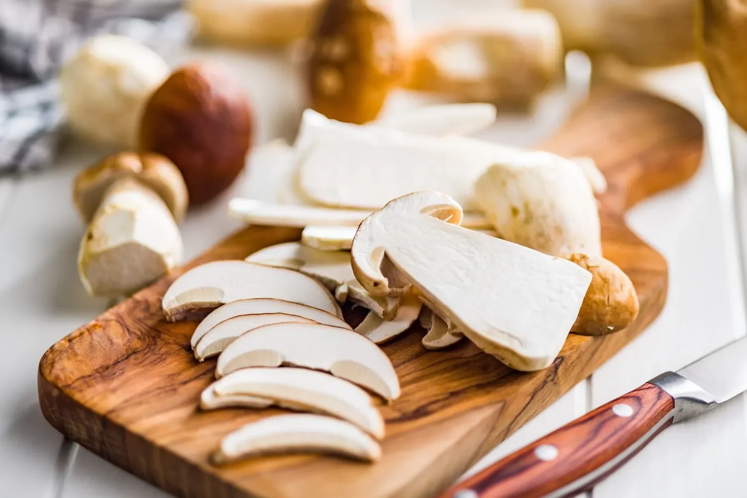 Cèpes émincés en lamelles régulières sur une planche en bois, couteau et cèpes entiers autour