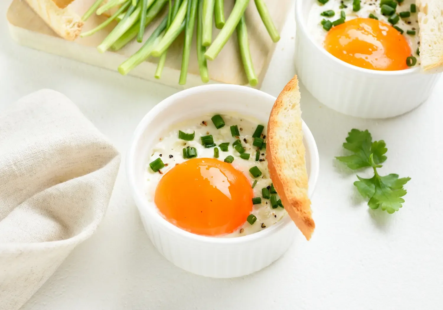 Deux ramequins d’œufs cocotte à la crème, jaune coulant, ciboulette et pain grillé.
